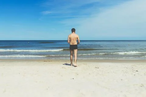 Young guy walking on an empty sandy beach towards the sea - silhouette of a y Stock Photos