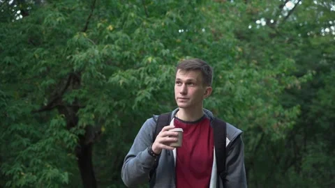 Young guy is walking in the park with a cup of coffee. sunset. Stock Footage 208876220