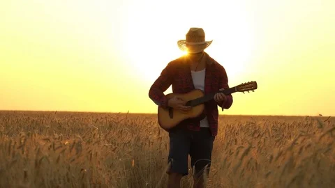 Young guy walks the golden wheat field in the rays of the sunset and plays the Stock Footage 79366763