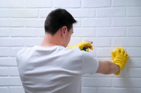 A young guy washes a brick, white wall. The guy cleans the house. Cleaning th Stock Photos