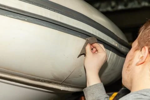 A young guy washes a cloth of an inflatable rubber boat of white color lifted Foto stock