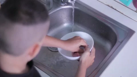 Young guy washes dishes in the sink in the kitchen. White plate in the frame clo Stock Footage 201662543