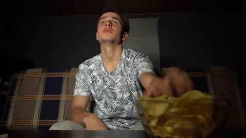 Young guy watching TV, eating chips, bored TV Stock Footage 126094015