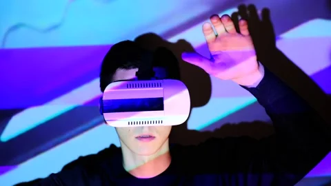 Young guy waving her arms in front of display. Man watches and using VR-helmet v Stock Footage 130180235