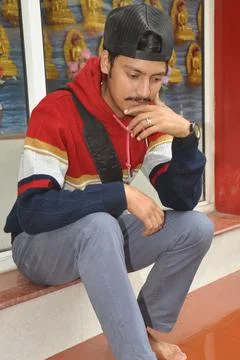 A young guy wearing cap backwards with looking down while sitting on stairs  Stock Photos