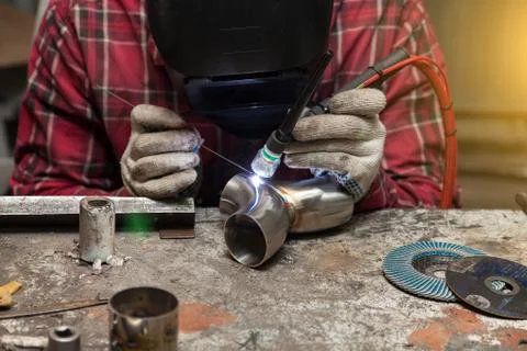 Young guy welder in a checkered red shirt welds a stainless steel pipe using  Stock Photos