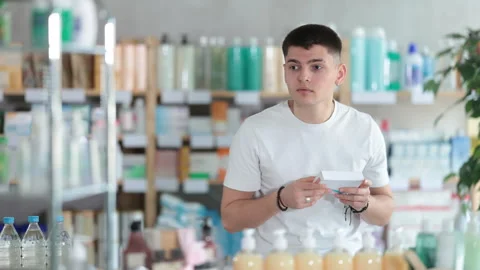 Young guy in a white summer t-shirt chooses boxes with pills and medicines Stock Footage 310682596