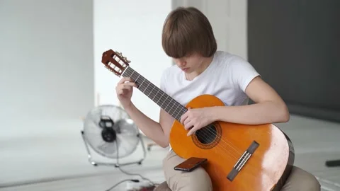 A young guy in a white T-shirt learns to play the guitar. Stock Footage 152790644