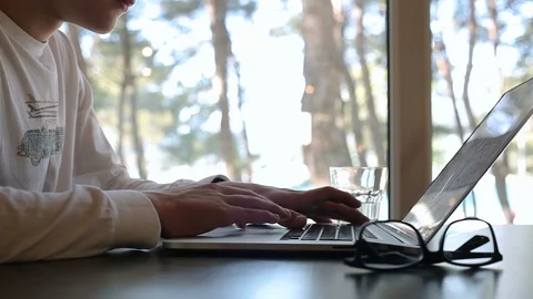 A young guy is working with a laptop in a cafe, glasses and a glass of water are Stock Footage 114123257