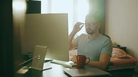 A young guy works remotely sitting at a table and writes notes on a computer. Video stock 236904242