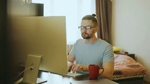 A young guy works remotely sitting at a table and writes notes on a computer. Stock Footage 238701025