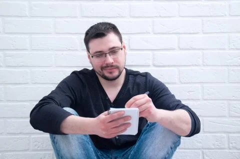 A young guy writes in a notebook, sitting on the floor against a white loft.  Stock Photos