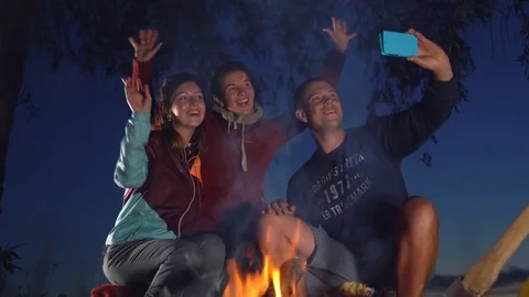 The young guys are sitting by the fire and doing a selfie photo Stock Footage 77732130