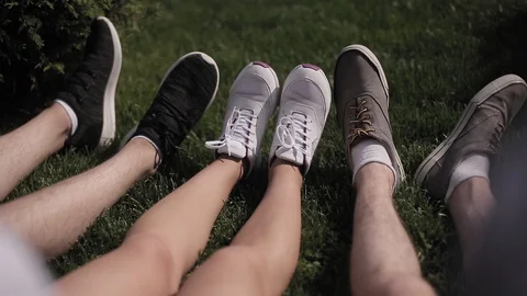 Young guys are sitting on the grass in the city. Close-up on the feet of youth Stock Footage 130135513
