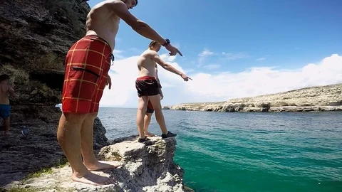 Young guys stand on the edge of the mountain and prepare to jump into the water Video stock 102019561