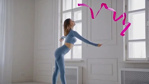 Young gymnast performs an exercise with a gymnastic ribbon in a light studio Video stock 145048247