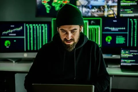 Young hacker man breaking into corporate servers from his home office Foto stock