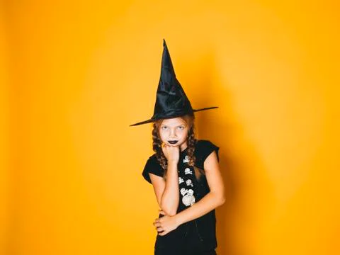Young halloween witch on orange background with black hat Stock Photos