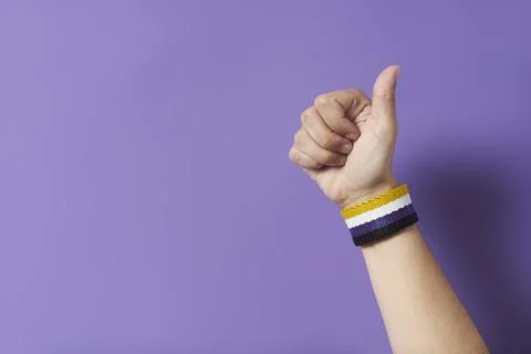 Young hand with a non binary flag bracelet with the thumb up. Gender diversit Stock Photos