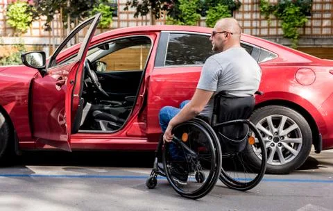 Young handicapped driver getting in red car fom wheelchair Foto stock