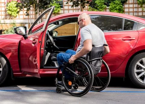 Young handicapped driver getting in red car fom wheelchair Stock Photos