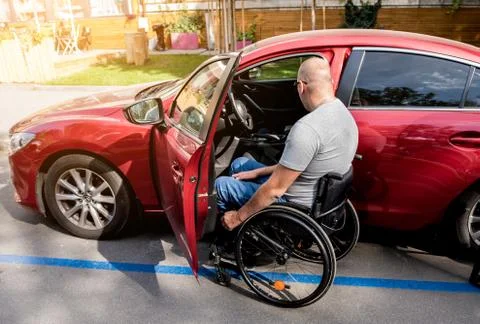 Young handicapped driver getting in red car fom wheelchair Stock Photos