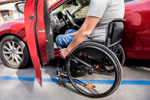 Young handicapped driver getting in red car fom wheelchair Foto stock