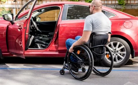 Young handicapped driver getting in red car fom wheelchair Foto stock