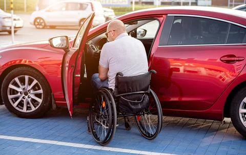 Young handicapped driver getting in red car fom wheelchair Stock Photos