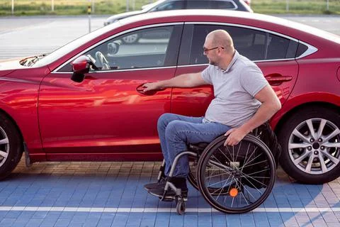 Young handicapped driver getting in red car fom wheelchair Stock Photos