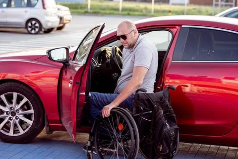 Young handicapped driver getting in red car fom wheelchair Foto stock