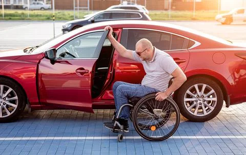 Young handicapped driver getting in red car fom wheelchair Foto stock
