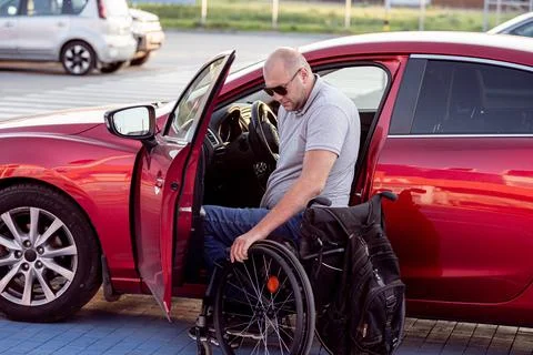 Young handicapped driver getting in red car fom wheelchair Foto stock