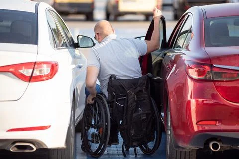Young handicapped driver getting in red car fom wheelchair Foto stock