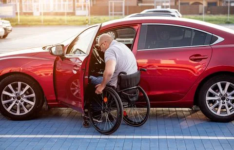 Young handicapped driver getting in red car fom wheelchair Stock Photos