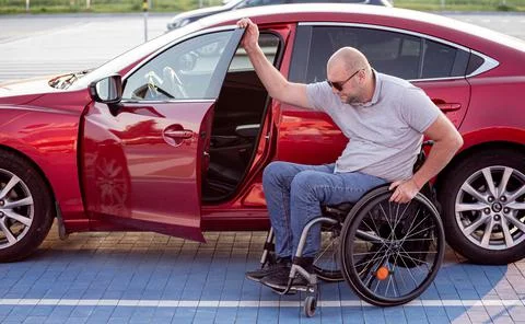 Young handicapped driver getting in red car fom wheelchair Stock Photos