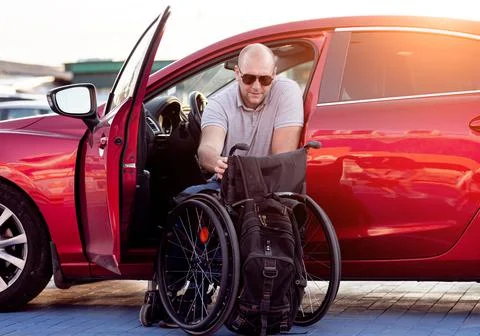 Young handicapped driver getting in red car fom wheelchair Stock Photos