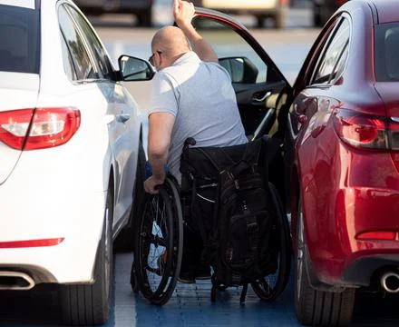 Young handicapped driver getting in red car fom wheelchair Stock Photos