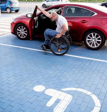 Young handicapped driver getting in red car fom wheelchair Foto stock