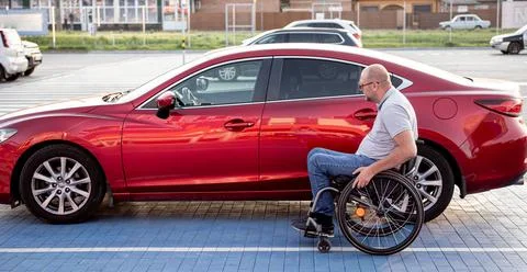 Young handicapped driver getting in red car fom wheelchair Foto stock