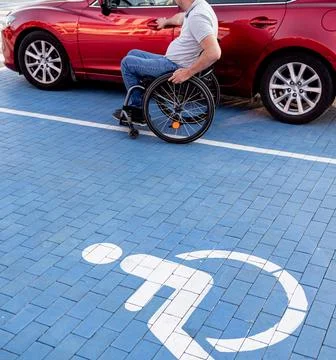 Young handicapped driver getting in red car fom wheelchair Foto stock