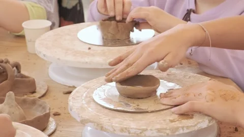 Young hands mold wet clay bowl on potter wheel during creative pottery class Stock Footage 343665860