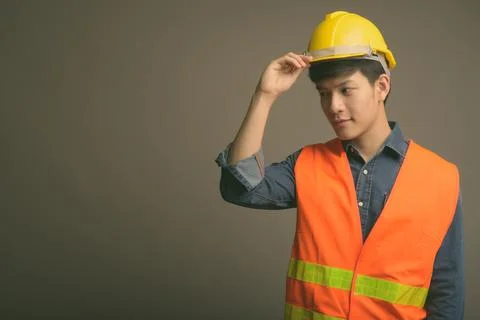 Young handsome Asian man construction worker against gray background Stock Photos