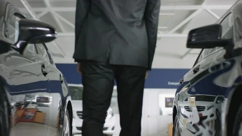 Young handsome auto dealer posing in car dealership. He is walking between new Stock Footage 127496485