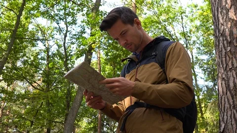 A young handsome backpacker examines a map in a forest - closeup from below Vídeos de archivo 109333102