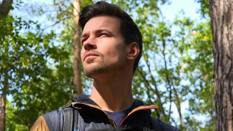 A young handsome backpacker stands in the middle of a forest and looks around - 스톡 동영상 109332818