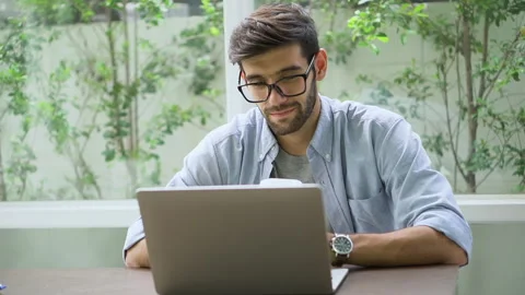 Young handsome bearded man freelancer sitting on desk using laptop computer a Stock Footage 134399386