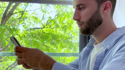 Young handsome bearded man texting on his smartphone while sitting Stock Footage 345117300