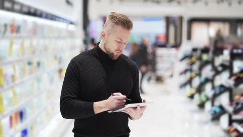 Young handsome bearded man uses digital tablet for work in shopping mall. Stock Footage 121951337