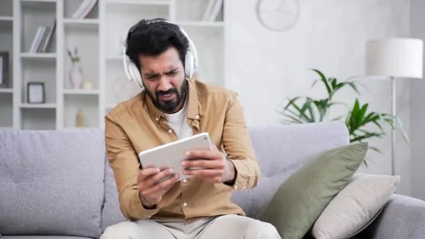 Young handsome bearded man in wireless headphones plays a computer game Stock Footage 252204315